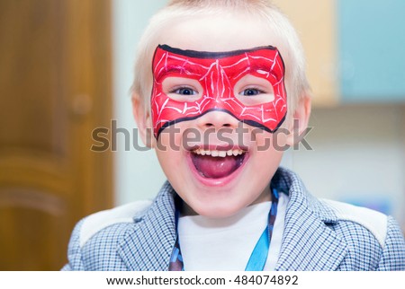 Excited caucasian boy with a spiderman mask on his face smiles at camera.
