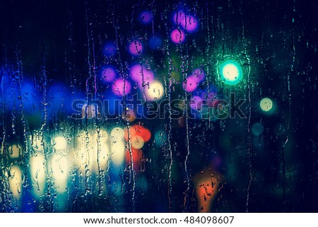Rain drops on car window with road light bokeh, City life in night in rainy season abstract background,water drop on the glass, night storm raining car driving concept.