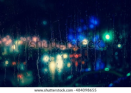Rain drops on car window with road light bokeh, City life in night in rainy season abstract background,water drop on the glass, night storm raining car driving concept.