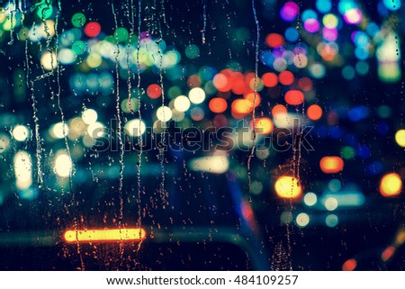 Rain drops on window with road light bokeh, City life in night in rainy season abstract background,water drop on the glass, night storm raining car driving concept.