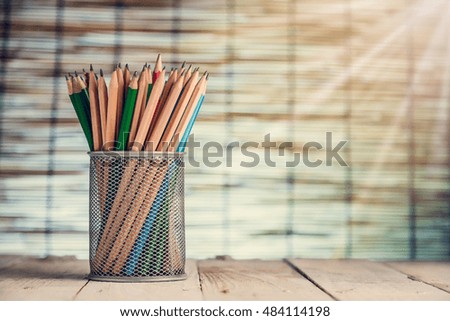 Group of pens and wooden pencils in metal vase on wooden floor