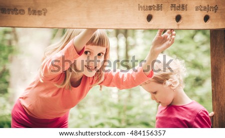 Two cute fair hair little girls - sisters learning from educational wooden board on nature trail. (Czech text: tento les? hustsi ridsi stejny - translation: this forest? denser, sparser, the same)