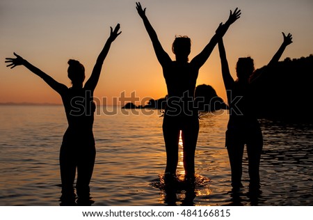 Happy friends on the beach in sea sunset. Silhouette sunset