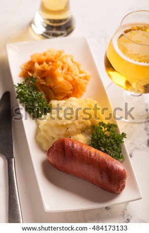 Grilled sausages and potatoes with glass of beer on the white surface