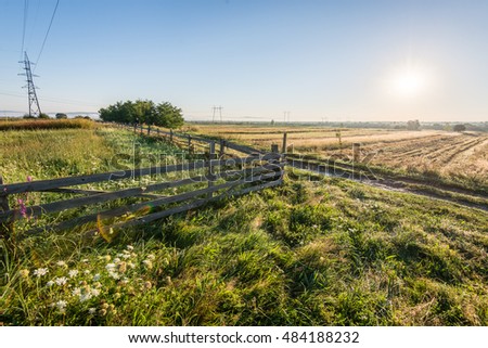 Winding country Road with clouds above and gravel surface and wooden fence
