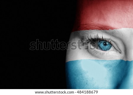 A young female with the flag of Luxembourg painted on her face on her way to a sporting event to show her support.