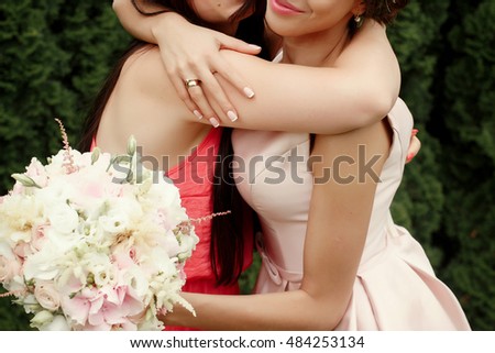 luxury bride hugging bridesmaid and smiling, joyful moment at reception, on background green wall of leaves, stylish wedding at botanical garden Royalty-Free Stock Photo #484253134