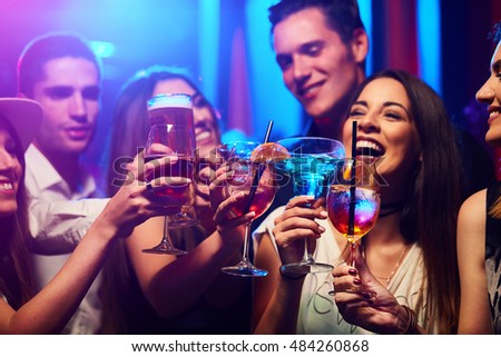 Young friendly people toasting in night club Royalty-Free Stock Photo #484260868