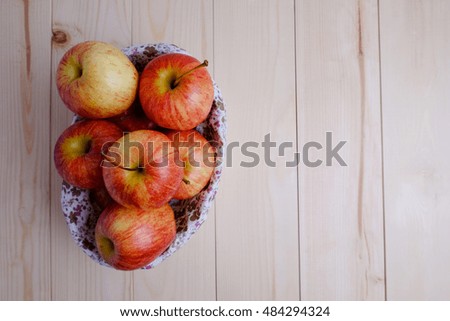 Top view of red apples in basket on wooden table, blank space and selective focus.