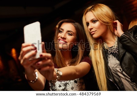 Two pretty girls take pictures at the club