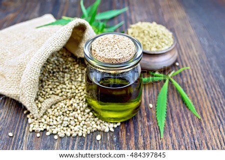 Hemp oil in a glass jar with flour in a clay bowl and grain in a bag, cannabis leaves and stalks on a wooden boards background Royalty-Free Stock Photo #484397845
