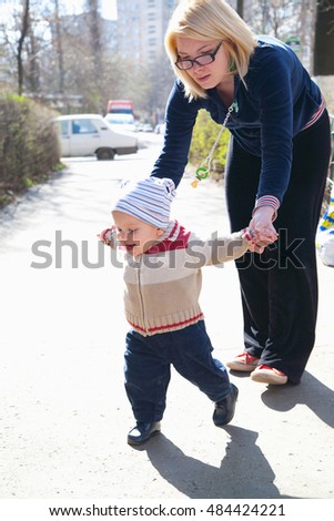 Baby learning to walk, mother helping him 