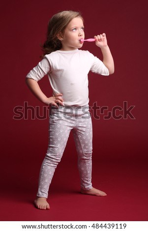Child brushing her teeth and posing. Red background