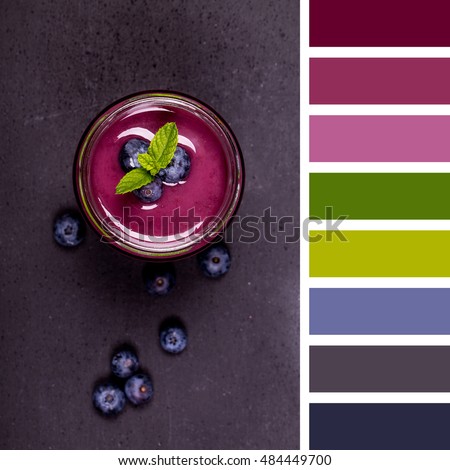 A blueberry smoothie with a sprig of mint and surrounded by fresh blueberries, in a glass jar with a straw and over a chalkboard background. In a colour palette with complimentary colour swatches.