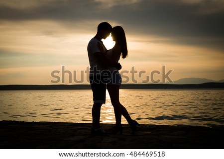 silhouette teenager lovers couple with sun between on sunset dusk sky background at the beach:black shadow hand drawn of people hug and kiss people:passion in love concept:decoration,design,valentines