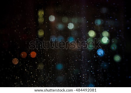 City view through a window on a rainy night,Rain drops on window with road light bokeh, City life in night in rainy season abstract background.
