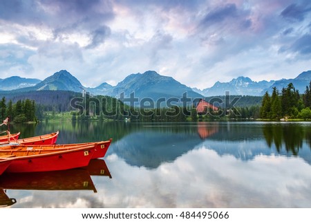 The picture captures the view of a person watching boats reverie, calm lake, fantastic mountains and the clouds floating across the sky