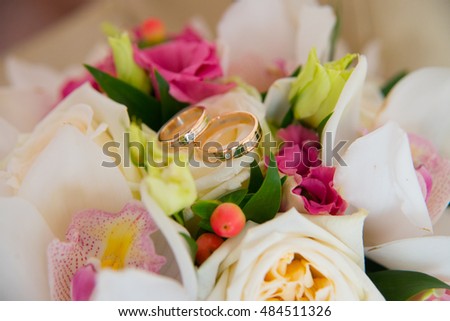 Two beautiful wedding gold rings with a diamond lying on the bride's bouquet of white orchids and pink flowers.