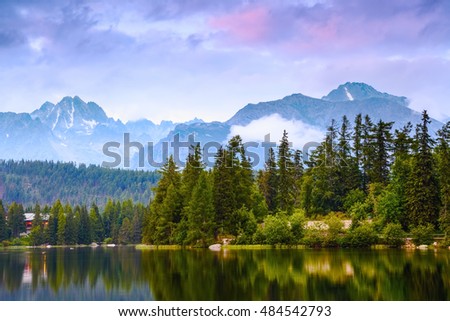 The picture captures the view of a person watching  calm lake, fantastic mountains and the clouds floating across the sky
