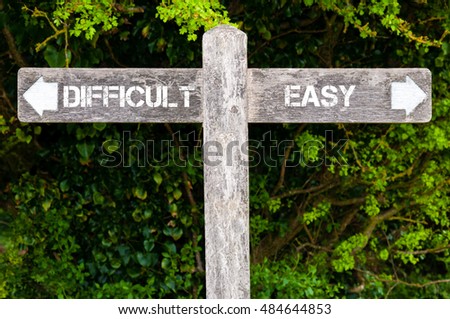 Wooden signpost with two opposite arrows over green leaves background. DIFFICULT versus EASY directional signs, Choice concept image Royalty-Free Stock Photo #484644853