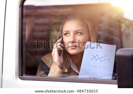 Serious business woman in the car going to work, analyzing graphics and discussing it on the phone, active morning of a business people