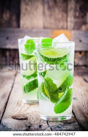 fresh mojito cocktails with lime, mint and ice in glass on wooden background