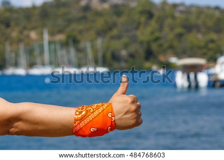 man's hand with raised thumb with orange bandana against the backdrop of marina Marmaris
