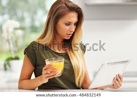 Picture of young woman with orange juice and tablet in kitchen