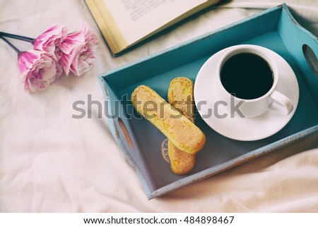 Dreamy image of romantic breakfast in the bed: cookies, hot coffee, flowers and open book. Vintage filtered and toned