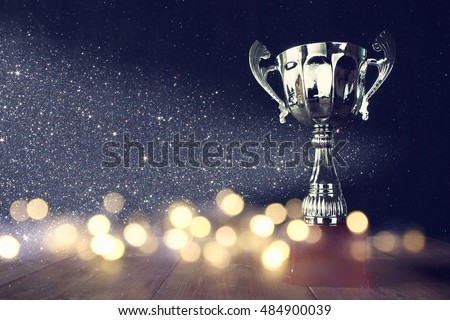 low key image of trophy over wooden table and dark background, with abstract shiny lights Royalty-Free Stock Photo #484900039