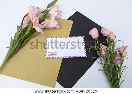 Composition with envelope and flowers. On envelope - the inscription Air Mail in English, French and Spanish. Photo background with white and black paper, craft paper. Natural backdrop for lettering