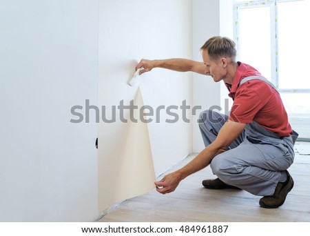 Worker pasting wallpapers. He presses for better adhesion using scraper. Royalty-Free Stock Photo #484961887
