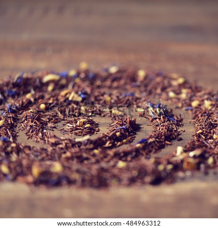 closeup of rooibos mixed with flowers, dry fruits and herbs, to prepare a rooibos tea, arranged forming circles on a rustic wooden table
