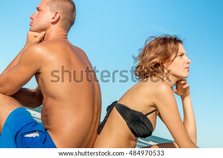upset couple sitting at the beach on vacation - angry young woman having an argument  disappointed with the man and looking away from each other -breaking up of a marriage and end of a love story