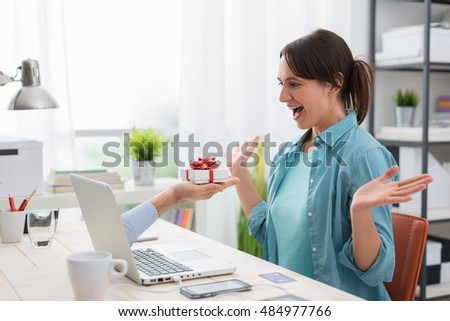 Cheerful young woman connecting to internet and receiving a present from a website, a male hand is coming out from the computer screen and giving her a gift box Royalty-Free Stock Photo #484977766