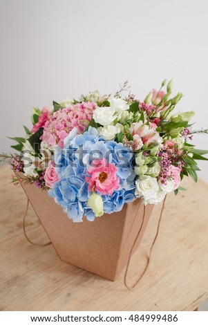 composition of different varieties roses and Serenity hydrangea. florist did rich bunch flowers light background, wooden surface. green vase in box