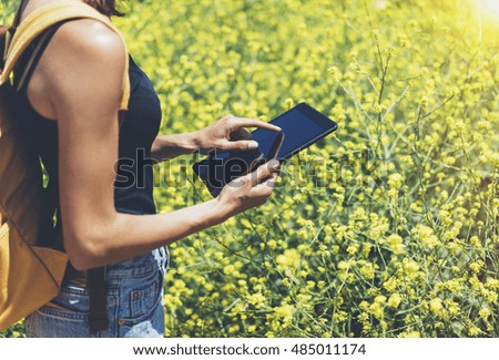 Hipster texting message on tablet computer, mockup of blank empty screen. Girl traveler using gadget on yellow flowers background close. Female hands photographer take view on cell camera