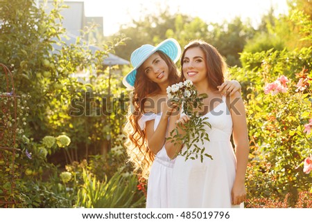 Two sisters. Girl holding a bouquet of flowers. Sister hugging her. In the backyard. Family time. Human relationships. Setting sun.