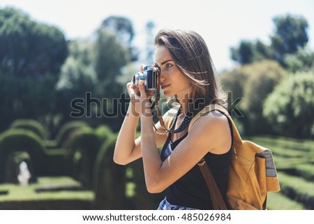 Hipster girl with backpack using vintage photo camera close up, copy space of blank empty mockup, view tourist holding in hands and photograph on device travel on background Barcelona park, sun flare