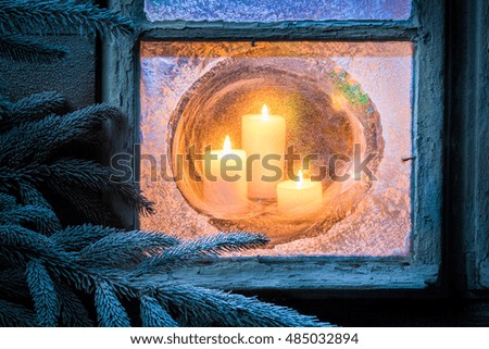 Stunning burning candles for Christmas in frozen window at eve