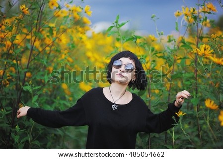 Young beautiful brunette girl in black clothes and sunglasses sneaking through the undergrowth of Jerusalem artichoke