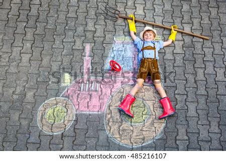 Happy little kid boy in straw hat and rain boots having fun with tractor picture drawing with colorful chalks. Children, lifestyle, fun concept. child dreaming of future and profession.