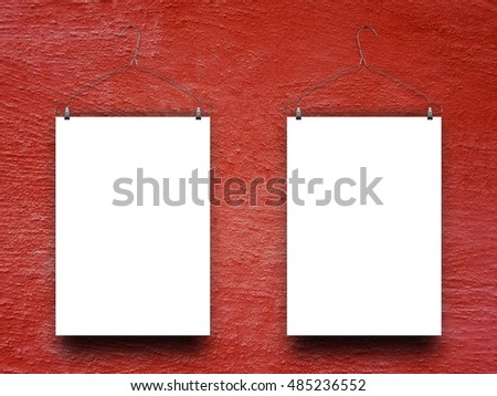 Close-up of two blank frames hanged by clothes hangers against red rough plastered concrete wall background