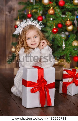 Girl with Christmas presents with the Christmas tree. Girl in white fur coat against the background of the Christmas tree. The holiday comes to us.