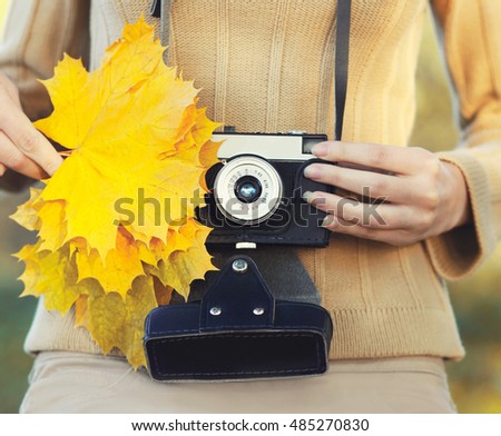 Autumn photo female hands holding retro vintage camera with yellow maple leafs closeup in warm day