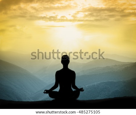 Yoga silhouette on the mountain in the rays of the dawn sun. Man meditates on nature.