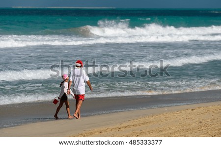 A man dressed as Santa Claus walking with his daughter on the beach during the Christmas holidays