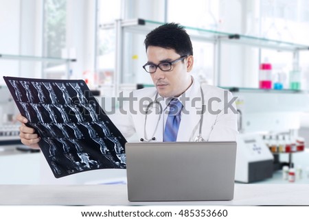 Picture of a male physician looking at x-ray or roentgen image with laptop on the table, shot in the laboratory