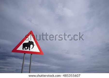 Danger elephant crossing road sign close to desert road with threatening sky in the background, Namibia, South West Africa