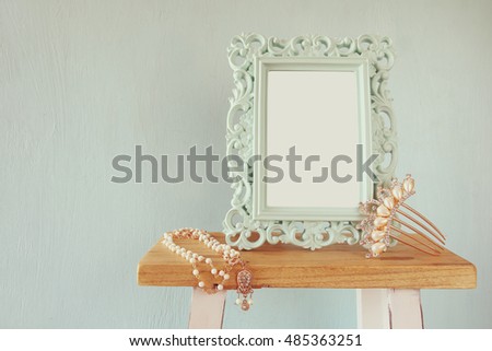 Blank victorian style frame, white pearls necklace and hair comb decoration on wooden table. Ready to photograph montage